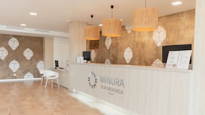 Un espace d’accueil avec un comptoir de réception en bois, deux lampes suspendues et une chaise blanche.