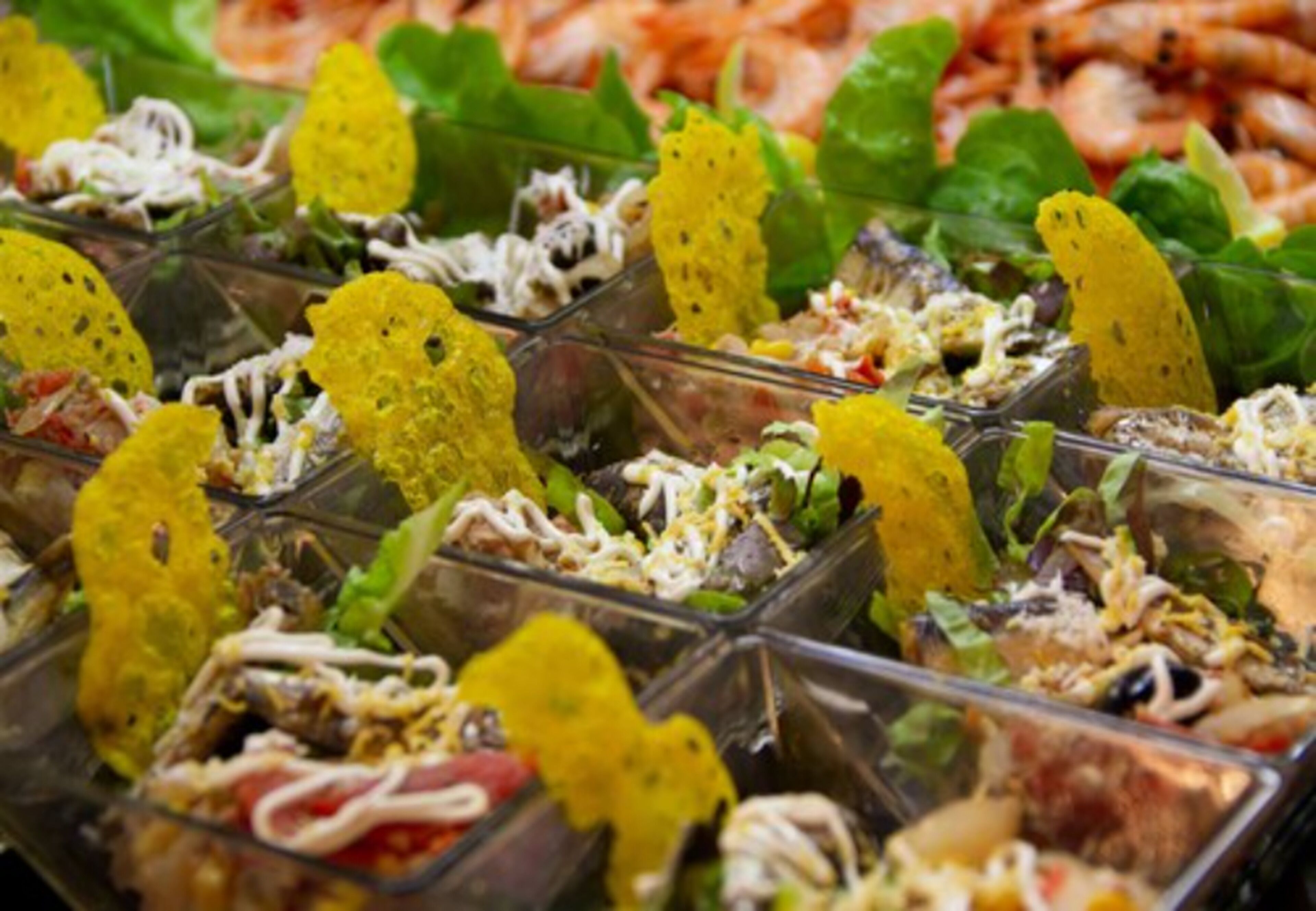 A variety of food items in clear containers, including salads and possibly some seafood, arranged on a table.