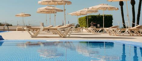 Un área de piscina con sillones de playa y sombrillas.