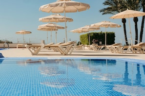 Una piscina al aire libre, sombrillas, sillones reclinables de piscina