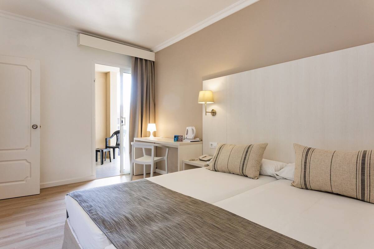 A hotel room with a large bed, a desk with a chair, a lamp, and a view of the hallway.