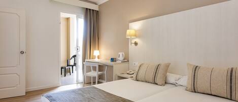 Habitación de hotel con una cama grande, un escritorio con silla, una lámpara y vistas al pasillo.
