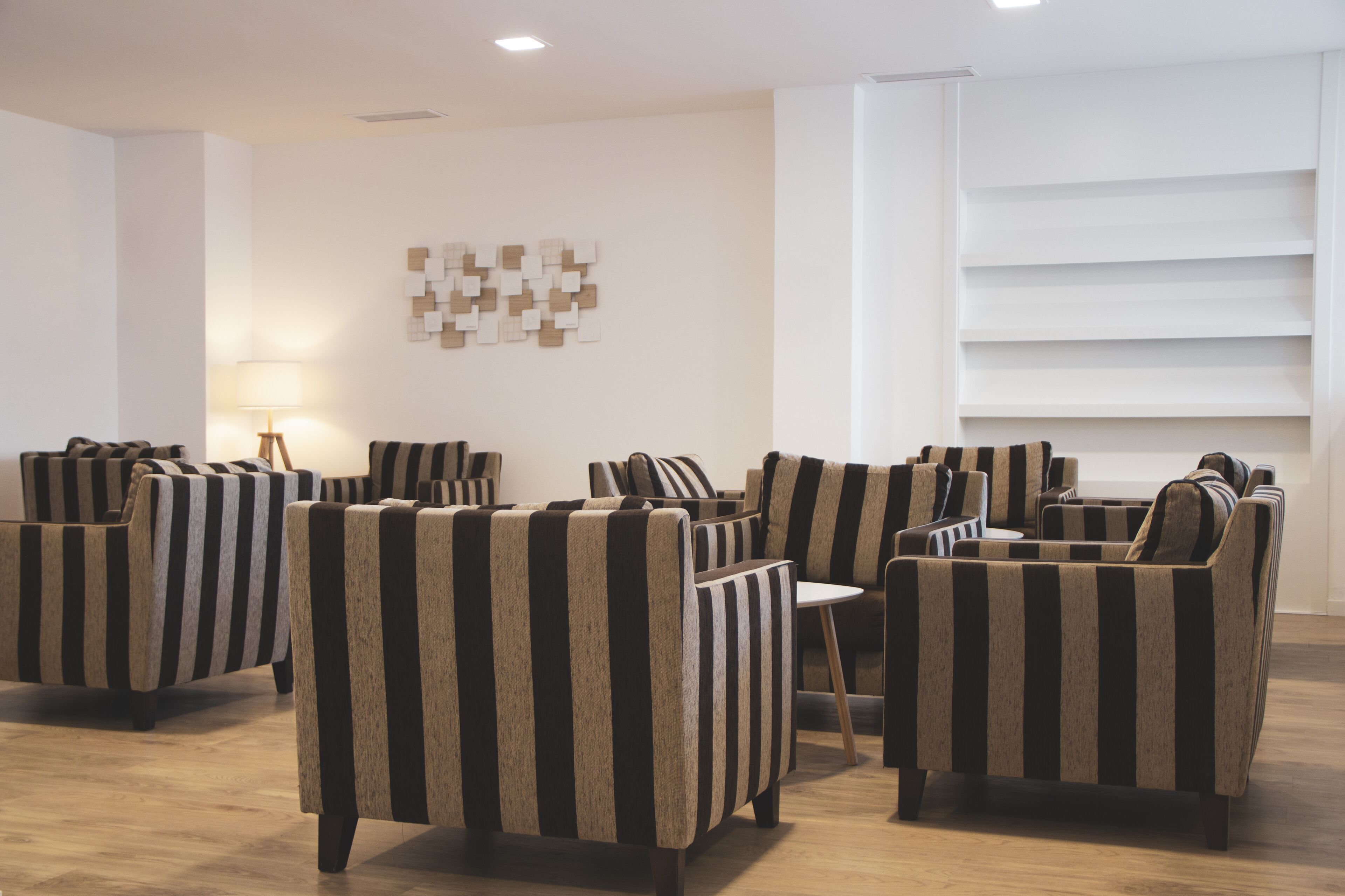 Un espacio lounge moderno con sillones a rayas y una pequeña mesa, una obra de arte abstracto en la pared y estanterías empotradas.