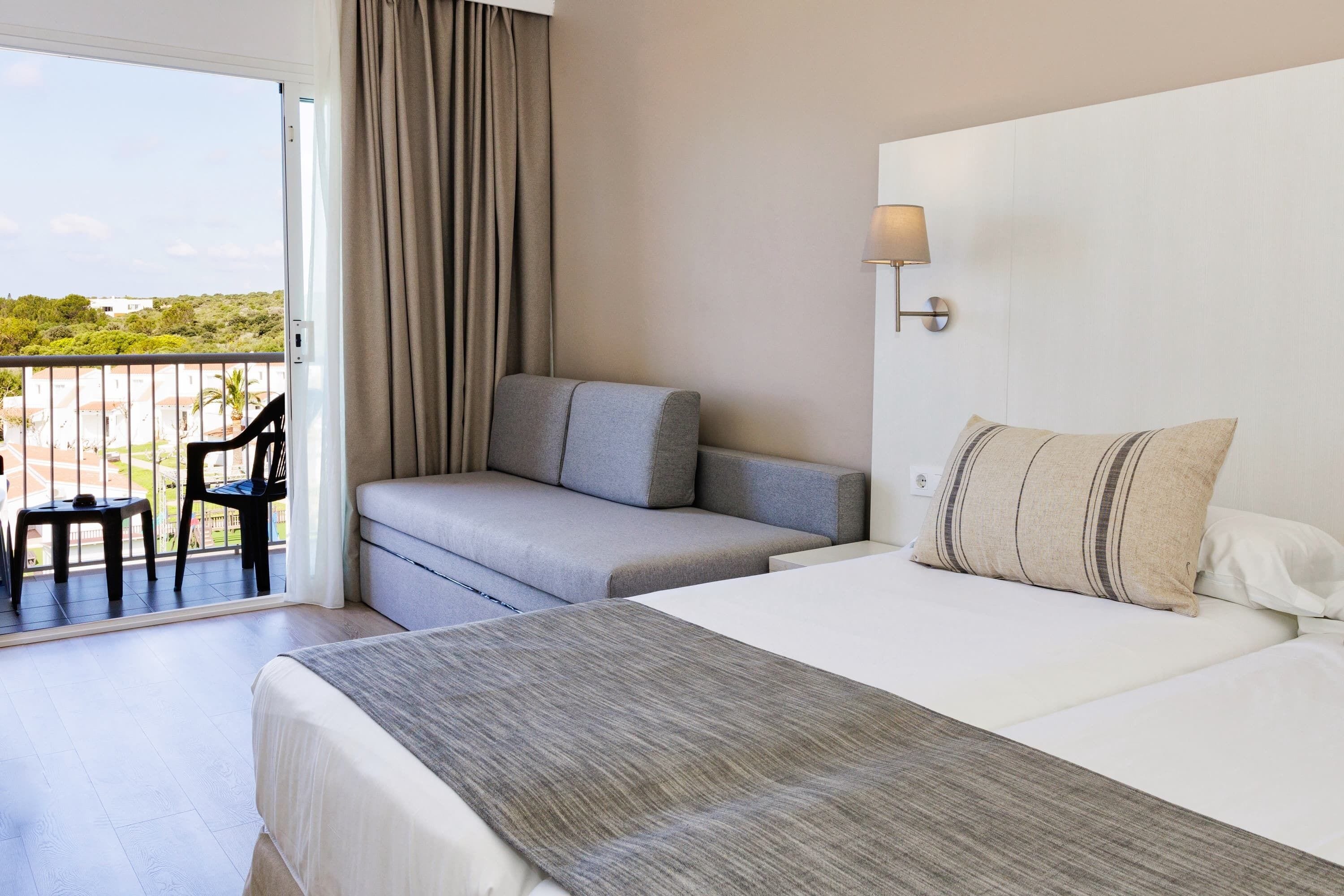 Una habitación de hotel con cama, sofá, sillón y balcón con vistas.