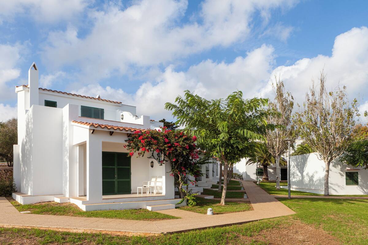A modern white building with a tiled roof, a covered patio with chairs, and a well-maintained lawn.