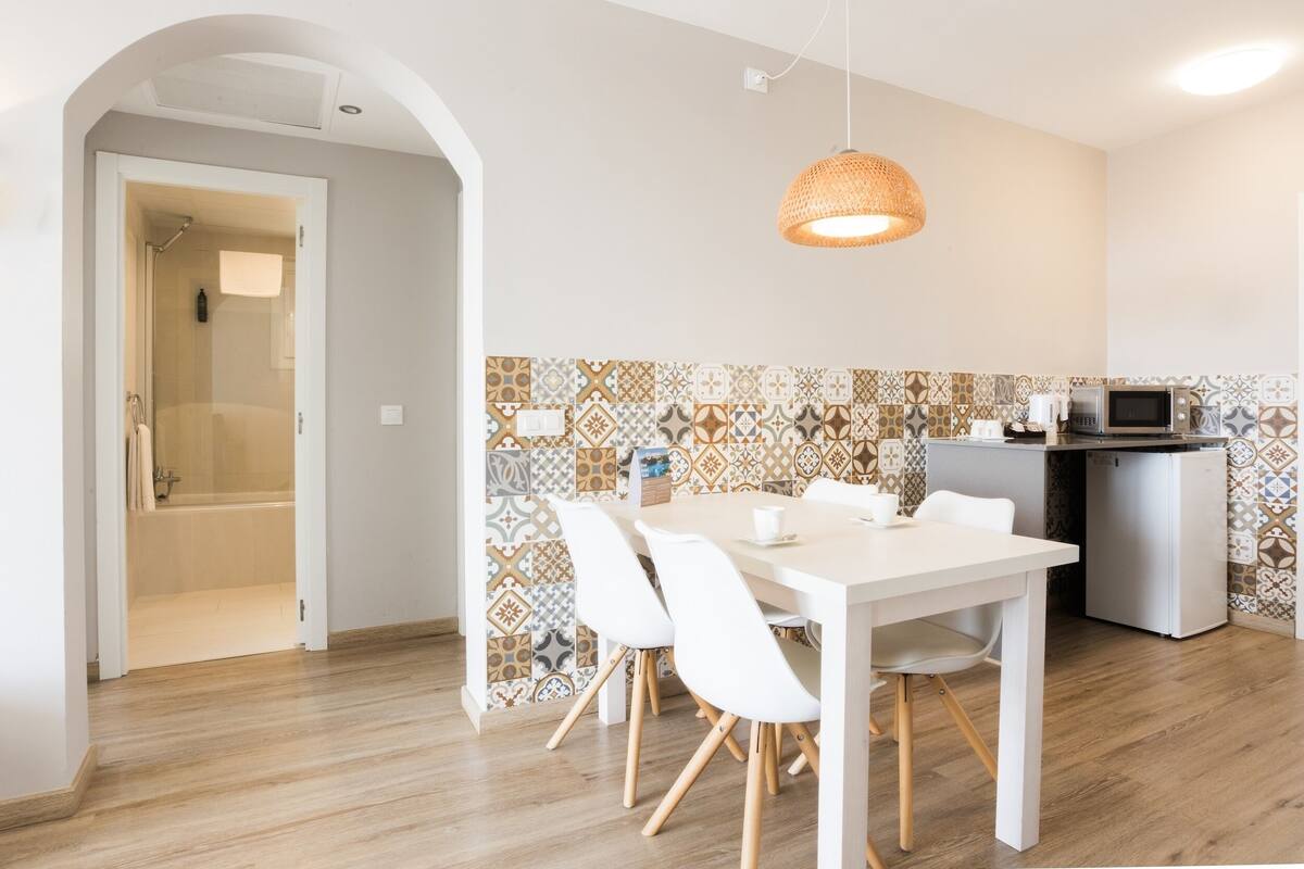 A modern kitchen with patterned backsplash, white dining table, and chairs, a microwave, and a small refrigerator.