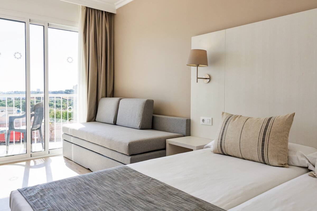 A hotel room with a bed, a sofa, a nightstand, and a lamp.