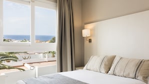Une chambre d’hôtel avec un lit, une fenêtre donnant sur l’océan, une lampe fixée au mur et un rideau.