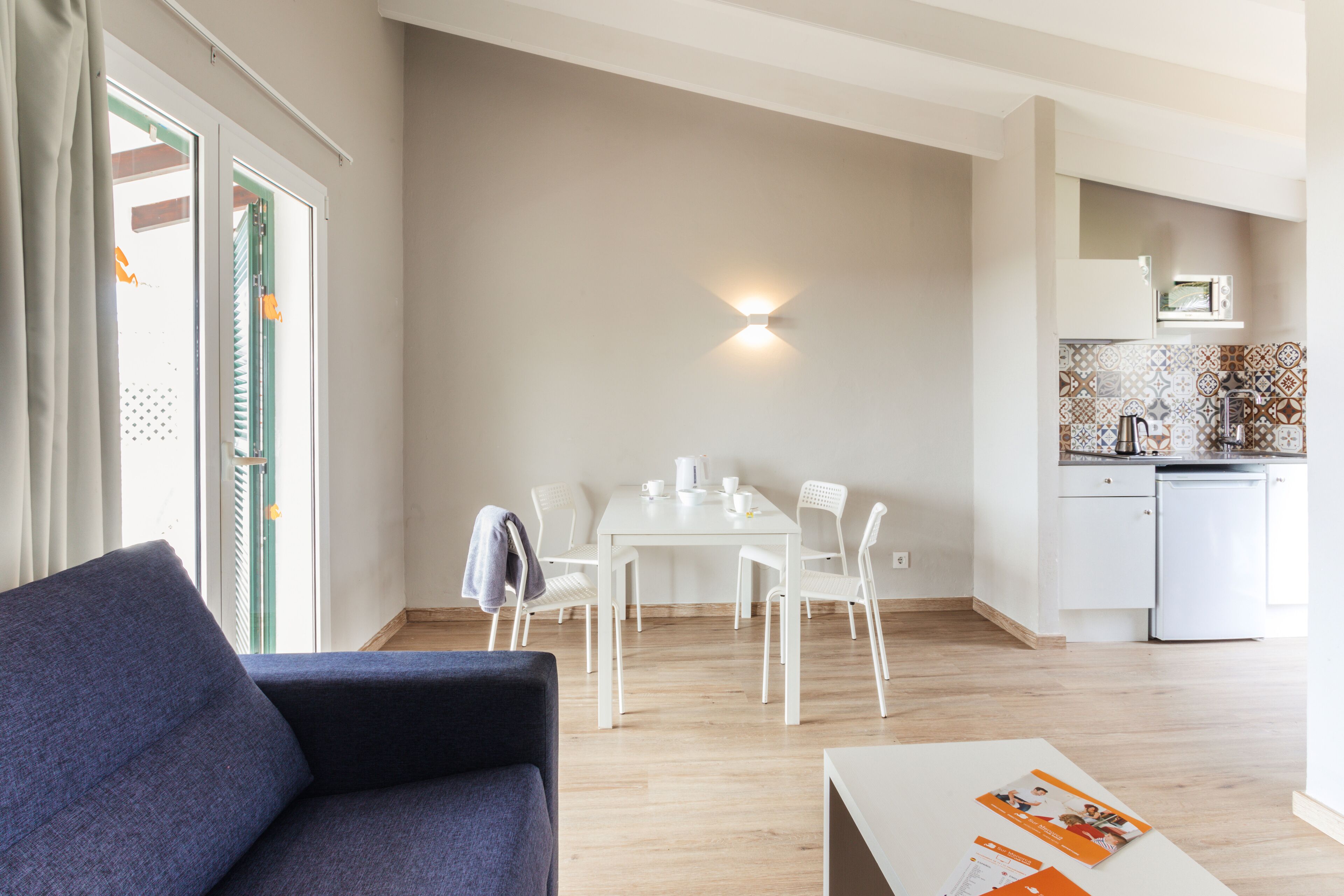 A modern living room with a sofa, a dining table with chairs, and a kitchen area with a microwave and sink.
