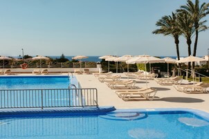 Una piscina al aire libre, sombrillas, sillones reclinables de piscina