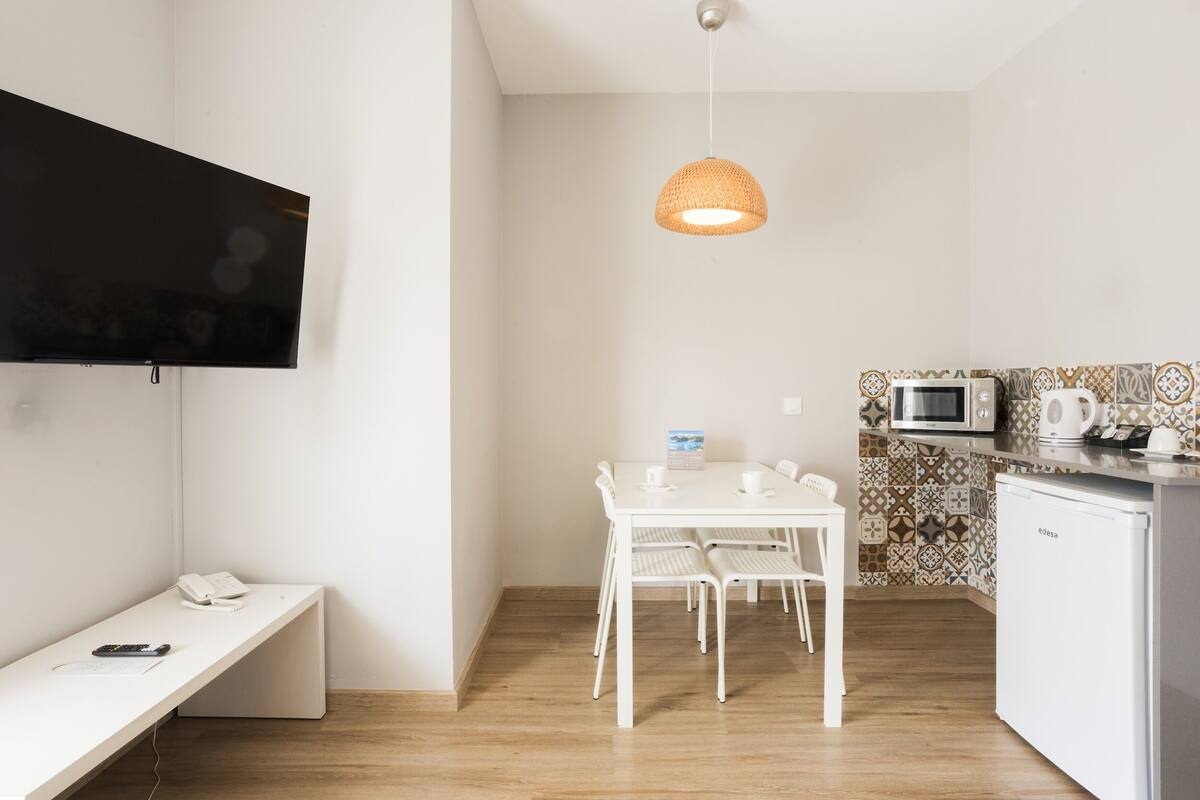 A small, modern kitchen with a white table, chairs, a microwave, and a refrigerator.