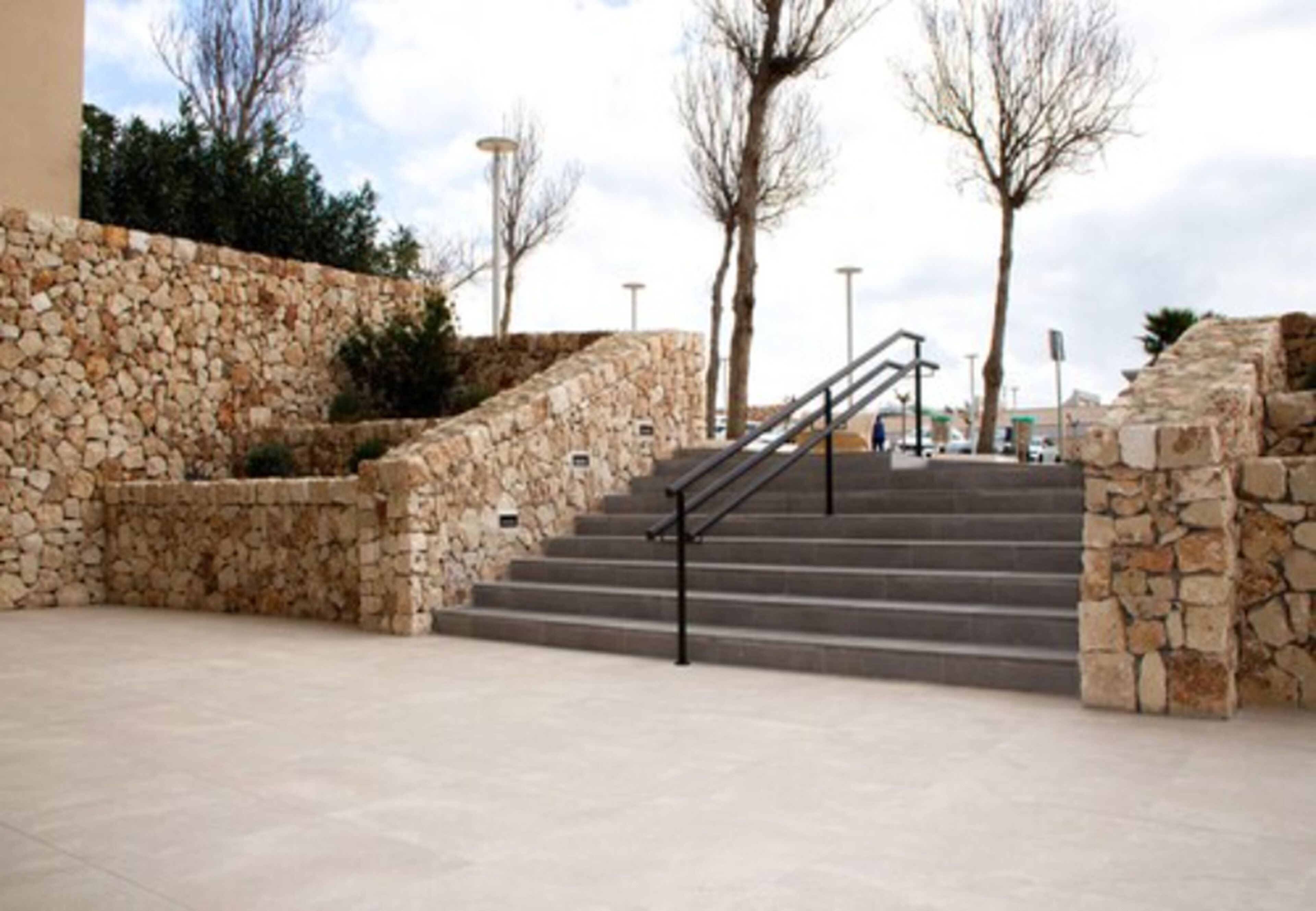 Una escalera de piedra que conduce a la entrada de un edificio, rodeada de un muro de piedra y árboles.