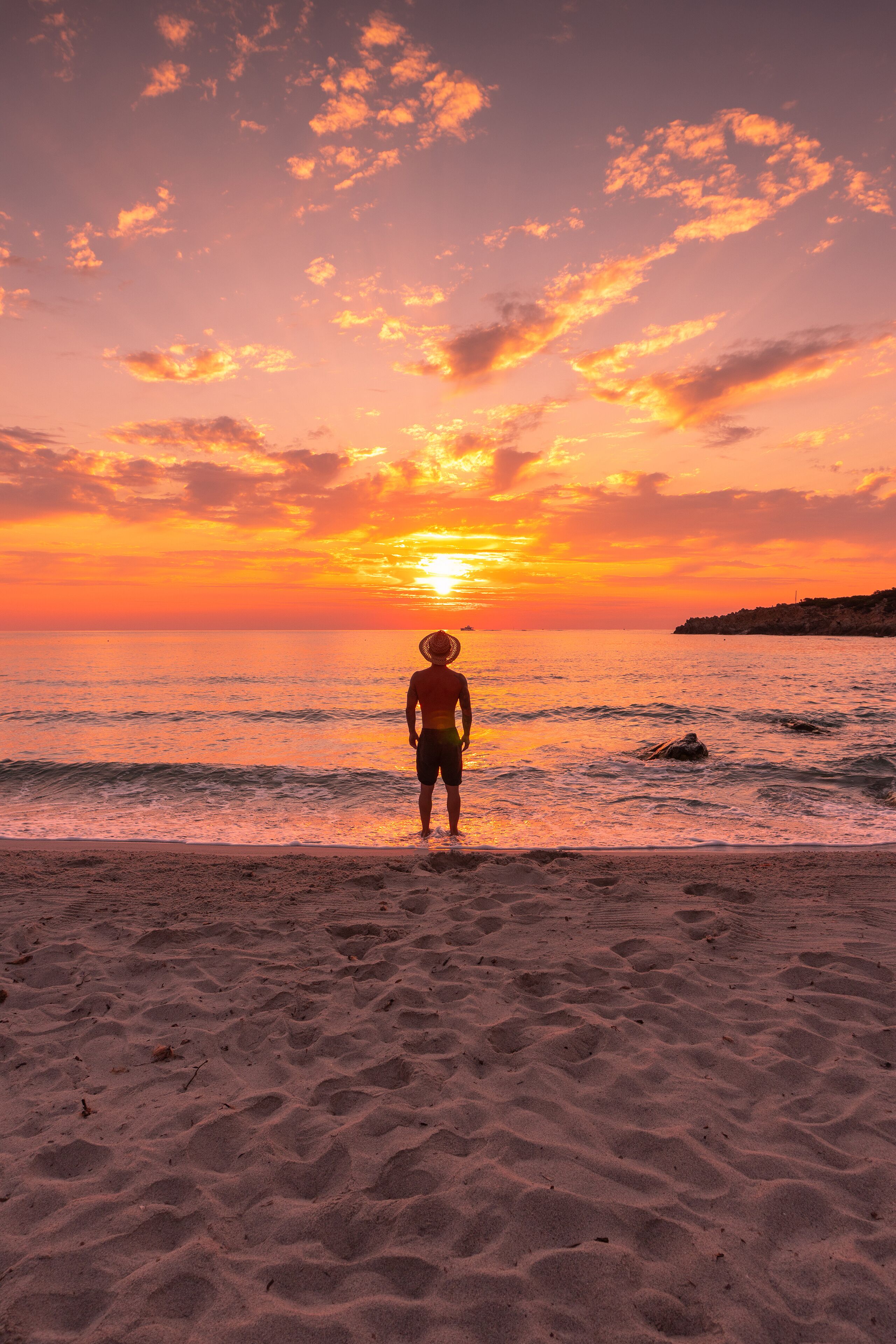 Una persona de pie en una playa arenosa mirando al atardecer sobre el océano.