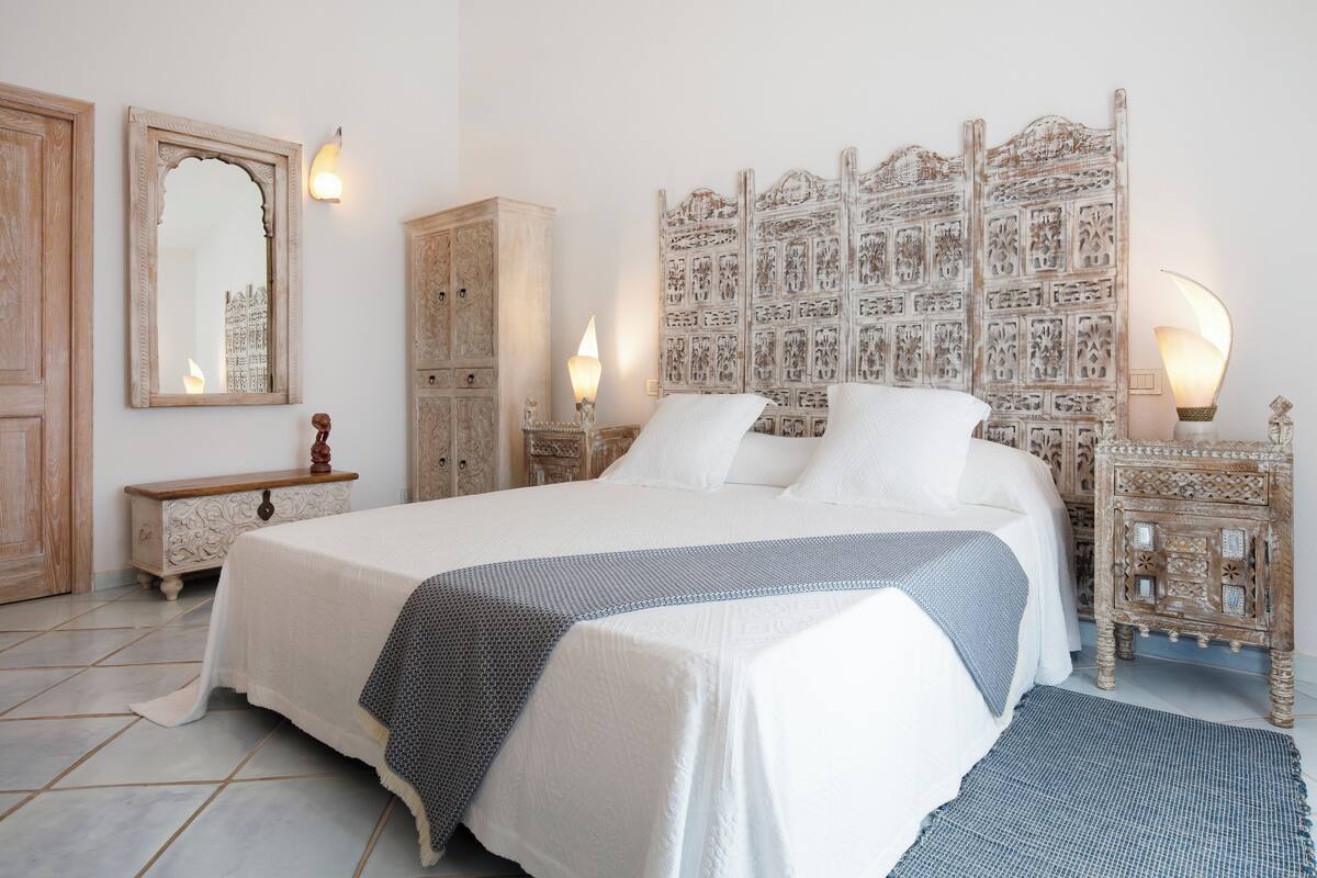 A neatly arranged bedroom with a large bed, a wardrobe, and a decorative headboard.