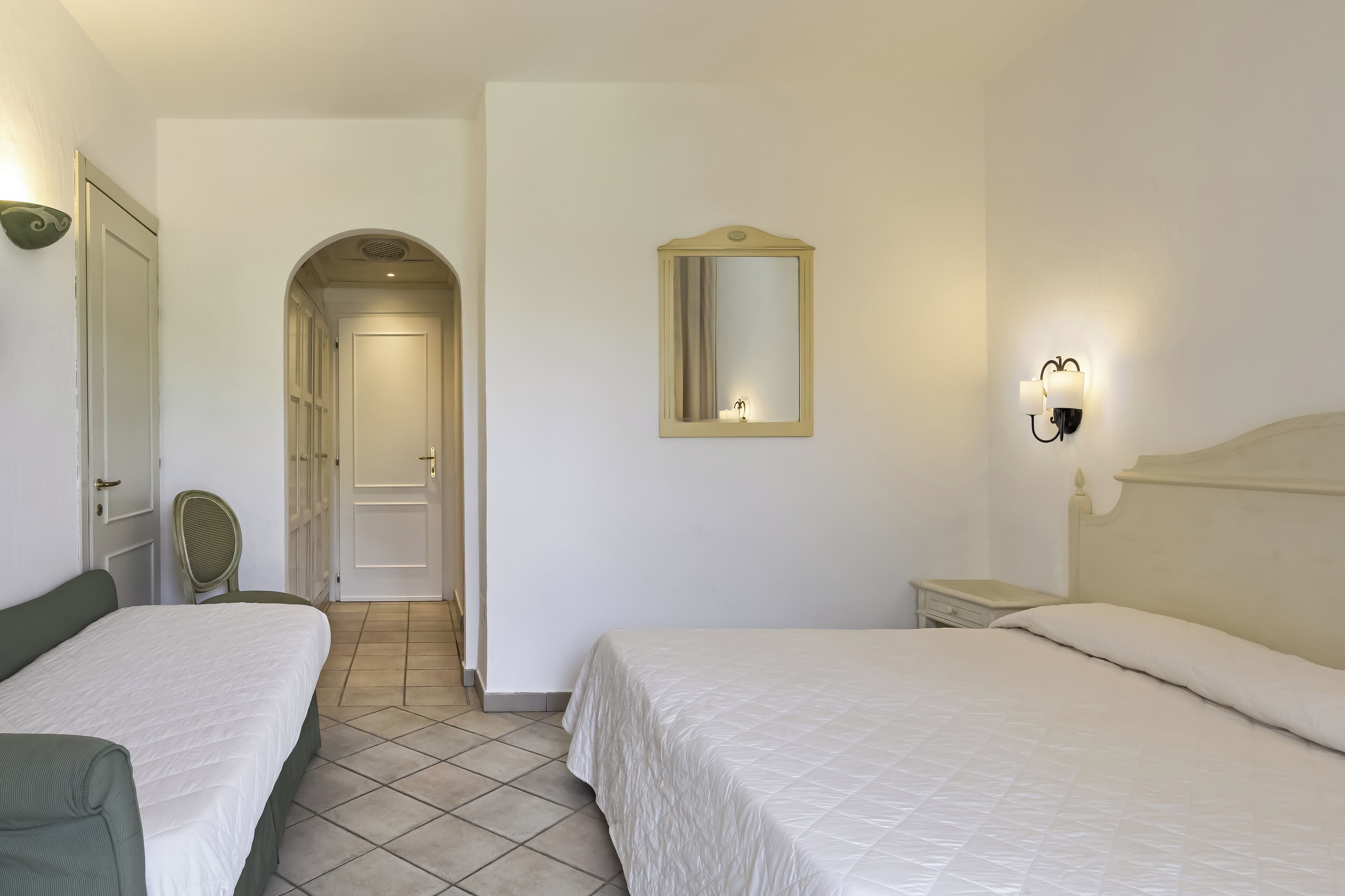 A hotel room with two beds, a mirror, a nightstand, and a chair.