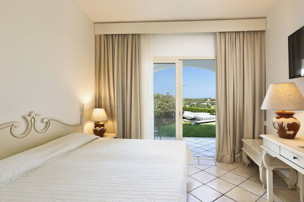 A hotel room with a bed, a desk, a lamp, and a view of the outdoors.