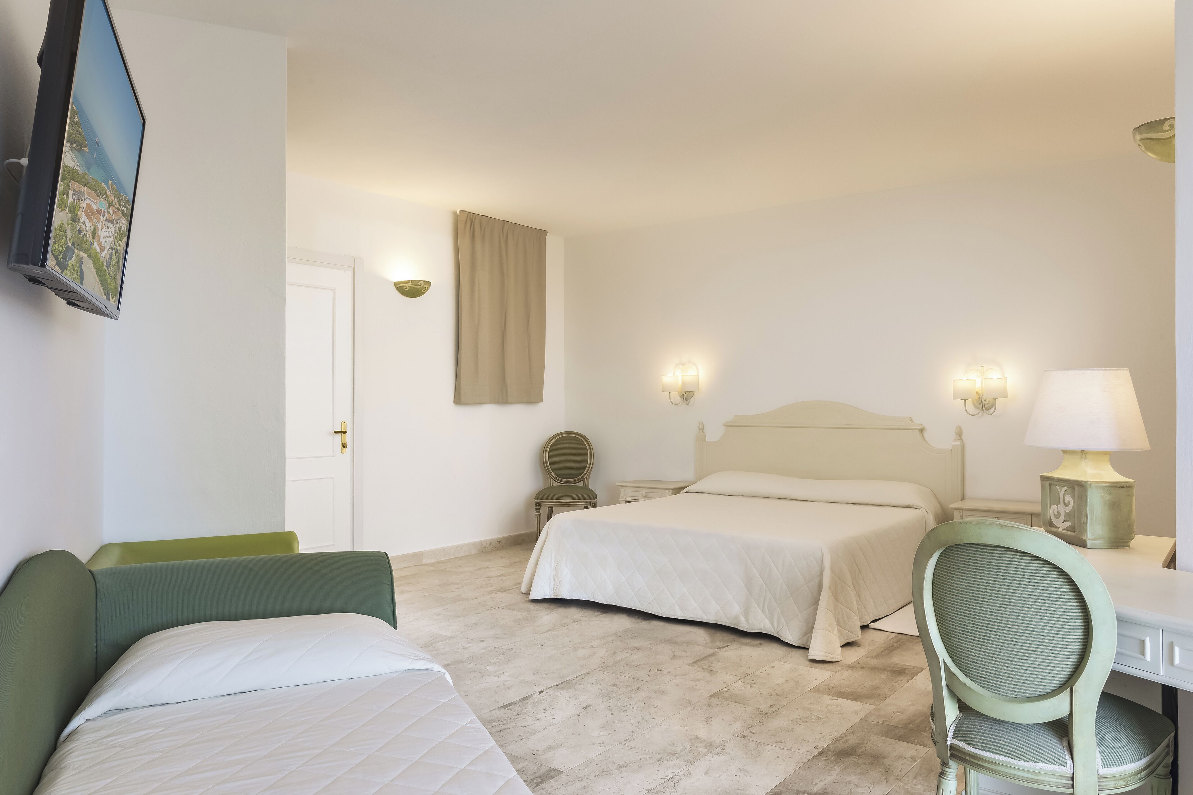 A hotel room with two beds, a desk, a chair, and a television mounted on the wall.