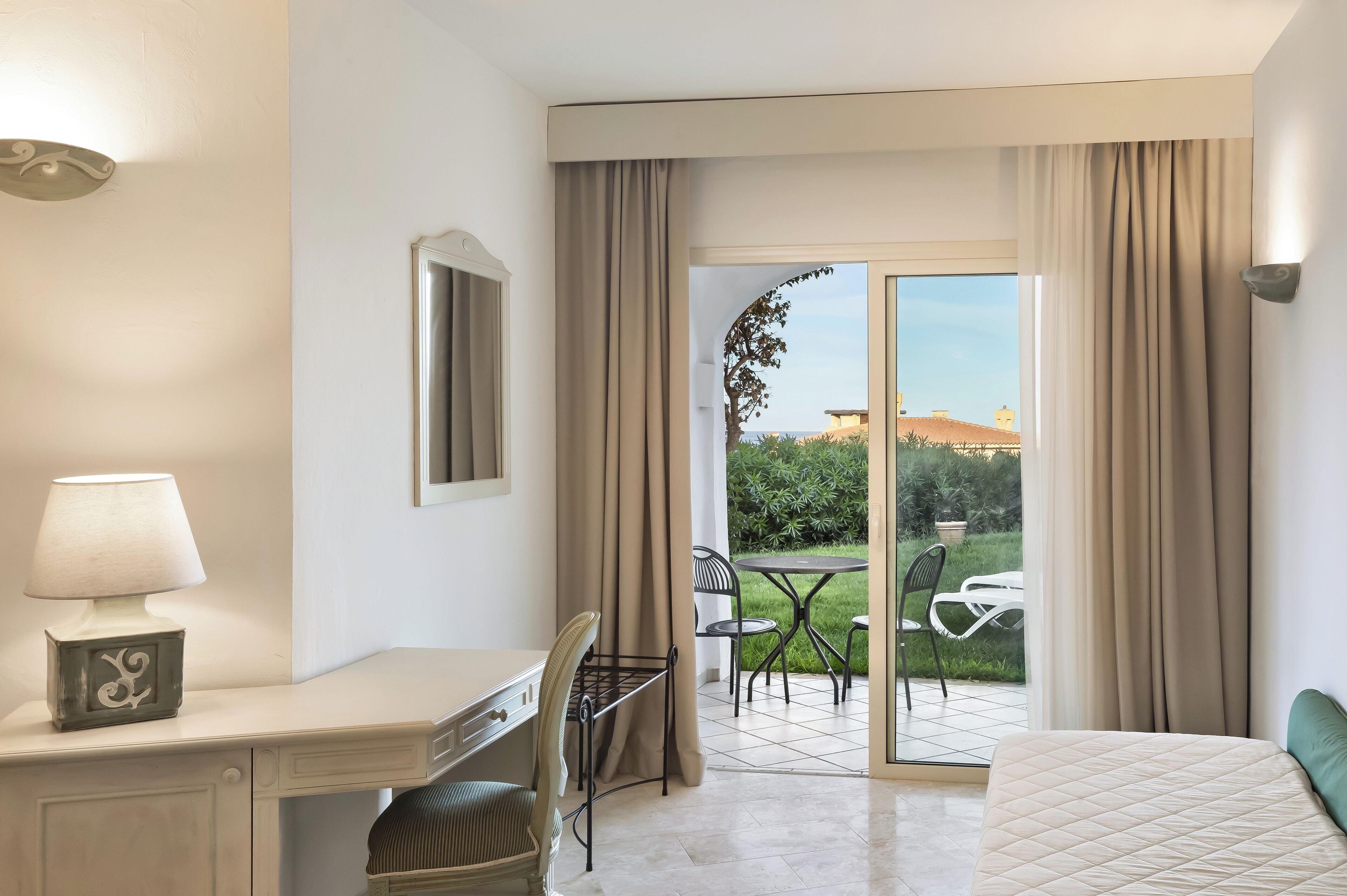 Une chambre d’hôtel équipée d’un bureau, d’une chaise, d’un lit et offrant une vue sur un jardin et un bâtiment à l’extérieur.