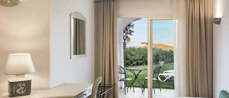 Une chambre d’hôtel équipée d’un bureau, d’une chaise, d’un lit et offrant une vue sur un jardin et un bâtiment à l’extérieur.