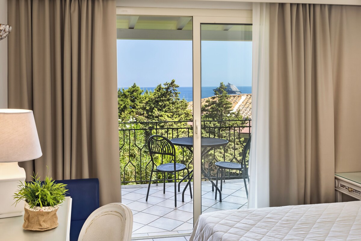 A hotel room with a balcony, a bed, a lamp, and a small plant.