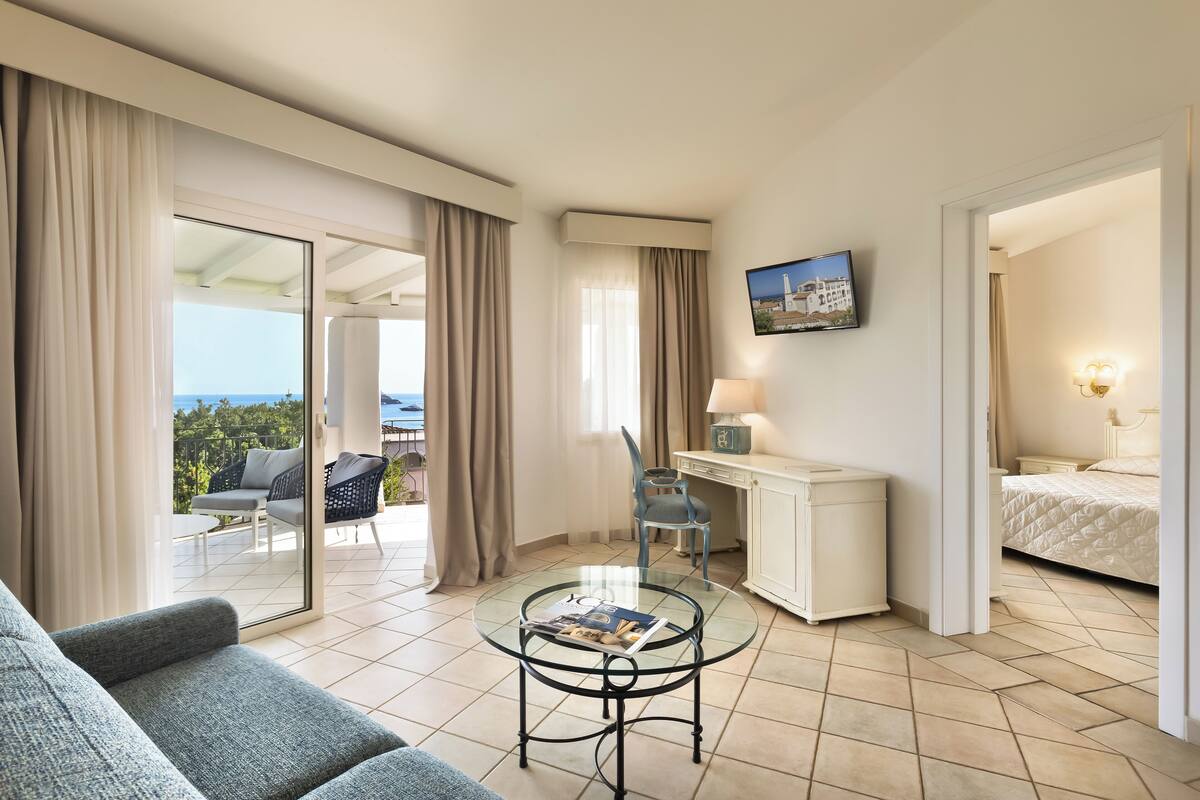 A hotel room with a balcony, a desk, a bed, and a sofa.