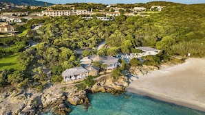 An aerial view of a coastal resort with multiple villas, a beach, and lush greenery. - Grand Hotel in Porto Cervo (Arzachena)