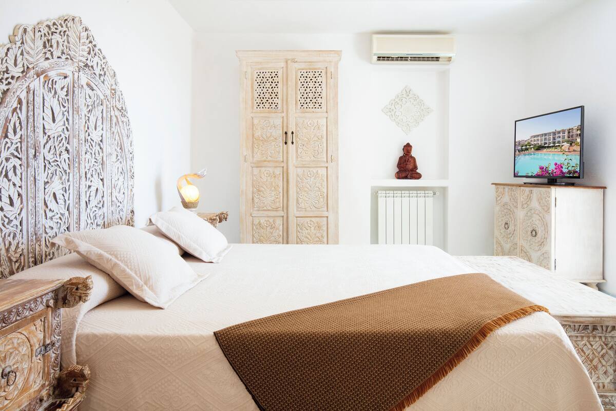 A bedroom with a large bed, a wardrobe, a television, and a decorative headboard.