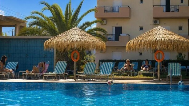 A swimming pool with lounge chairs and thatched umbrellas, surrounded by a multi-story building with balconies. - Castro Hotel (Malevizi)
