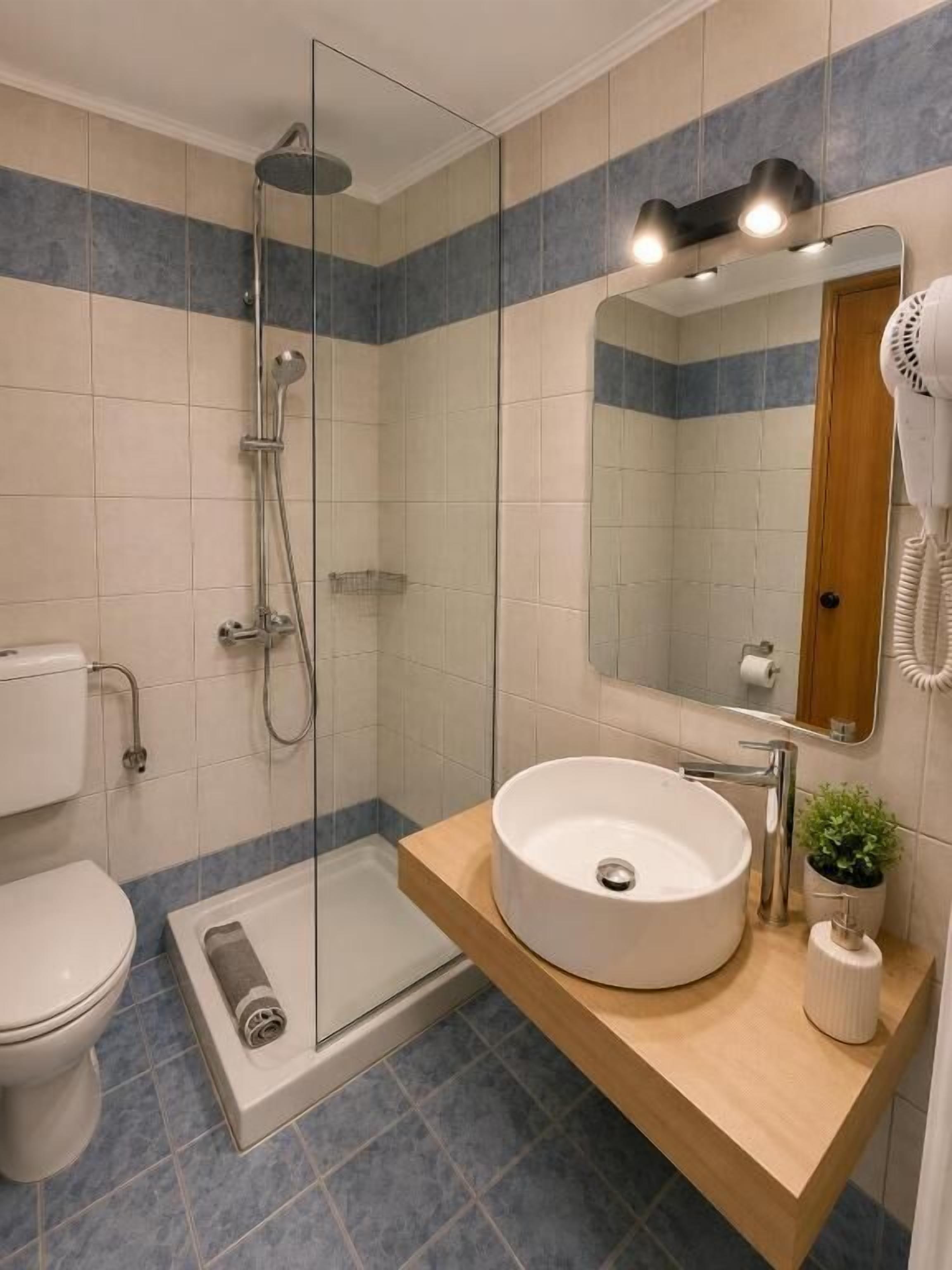 A bathroom with a glass-enclosed shower, a white sink, a mirror, and a hairdryer.