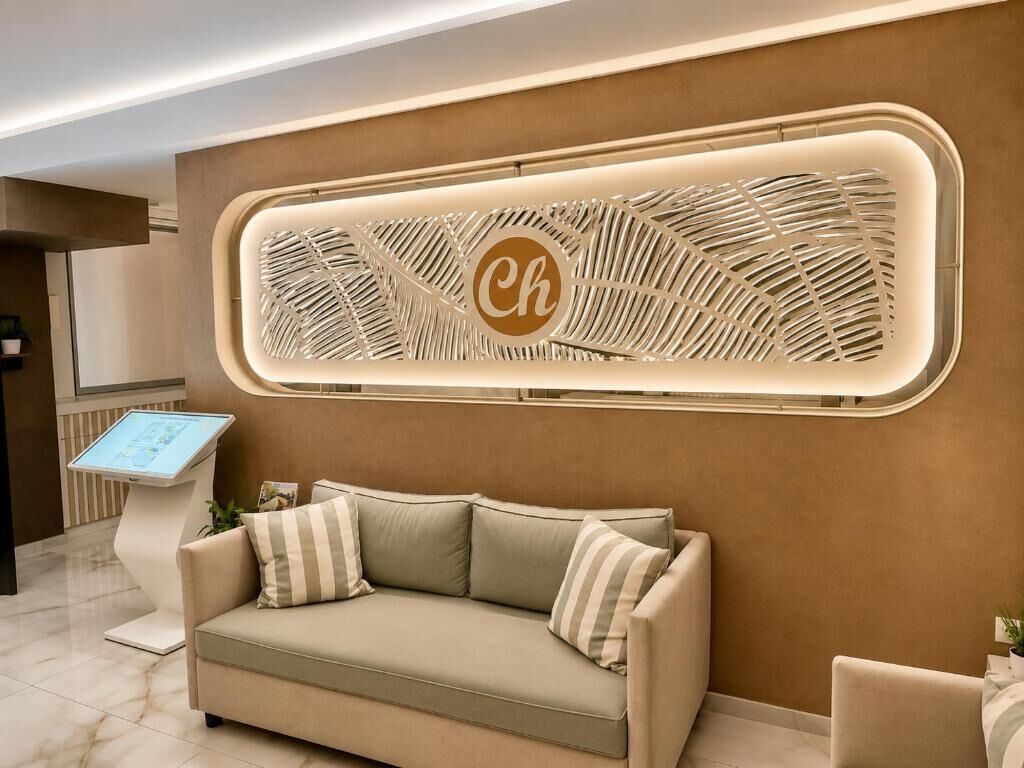 Een receptiegedeelte met een bank, een digitale kiosk en een decoratief wandobject met de letter 'Ch'.
