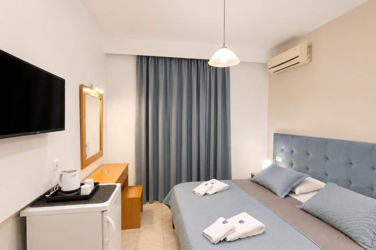 A hotel room with a bed, a TV, a desk with a kettle, and a window with curtains.