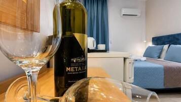 Una habitación con una mesa de madera, dos copas de vino, una botella de Metaxa y una cama con cabecera azul.