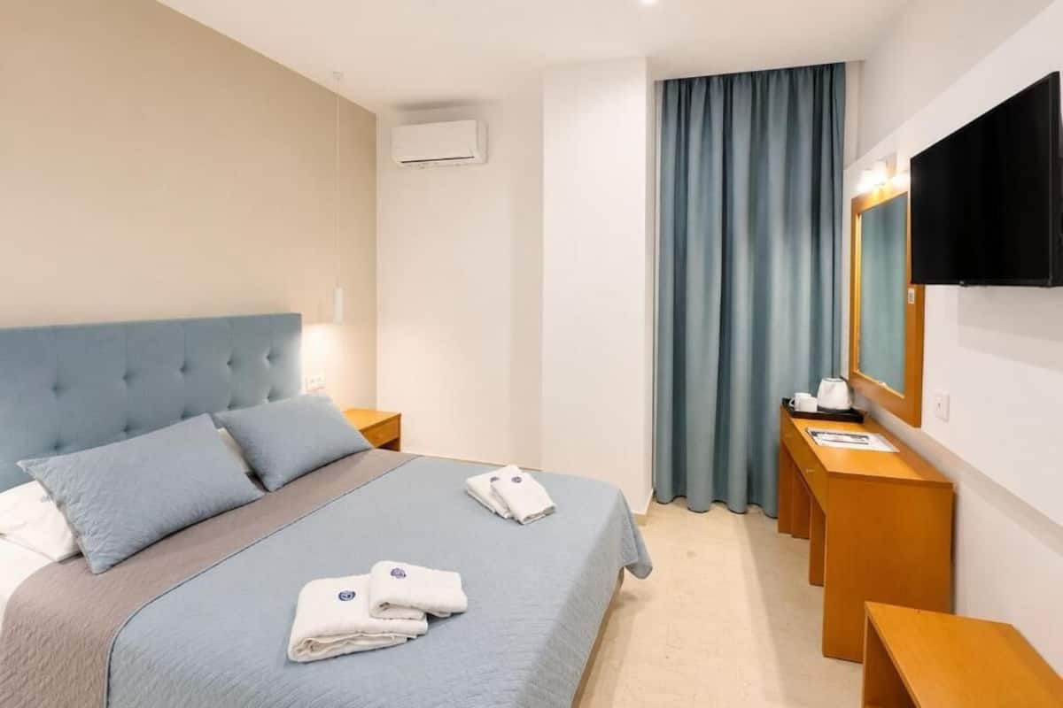 A hotel room with a bed, a desk, a television, and a window with curtains.