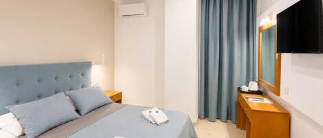 Habitación de hotel con cama, escritorio, televisor y ventana con cortinas.