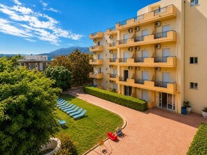 A multi-story hotel with balconies, a courtyard with lounge chairs, and a clear view of mountains in the background. - Castro Hotel (Malevizi)