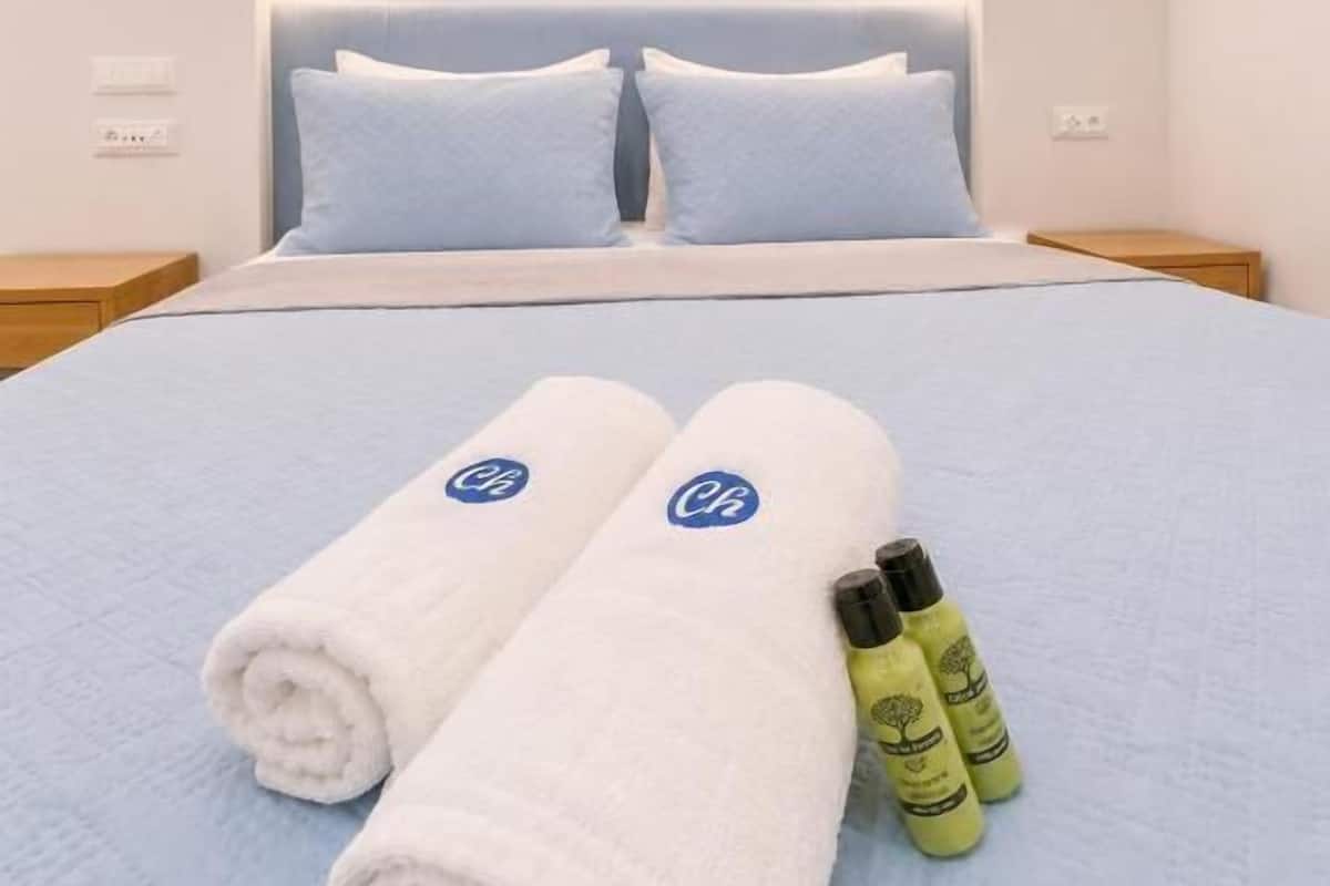 A hotel room with a bed, two pillows, two rolled towels, and two bottles on the bed.