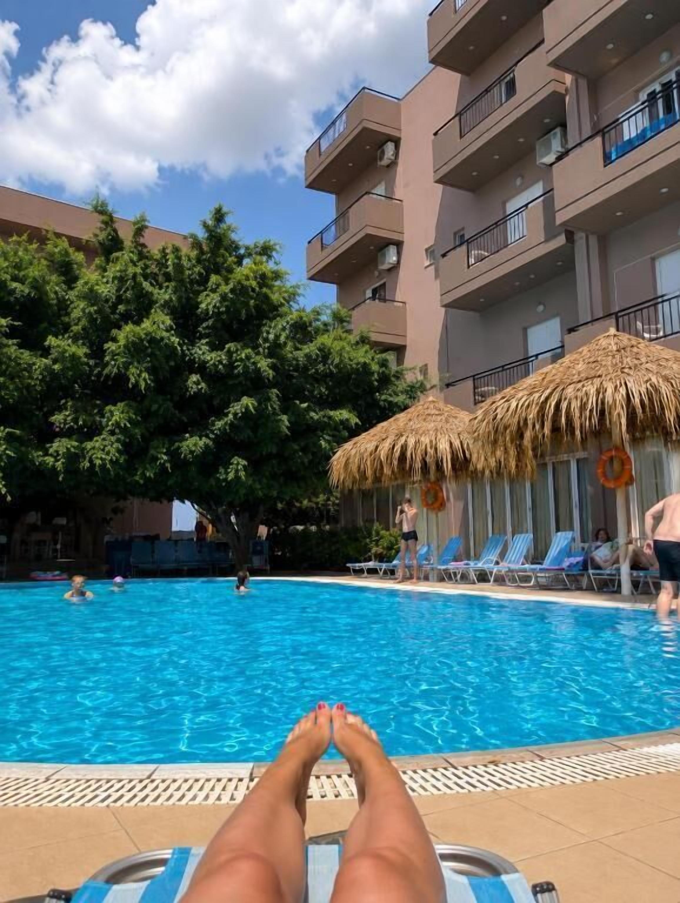 A swimming pool with lounge chairs and umbrellas, surrounded by trees and a multi-story building.
