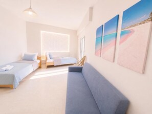 A modern hotel room with a sofa, two beds, a large window, and beach-themed artwork. - Castro Hotel (Malevizi)