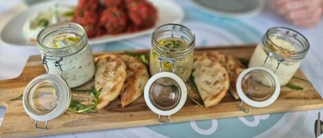A wooden board with jars of dips and flatbread on a table.