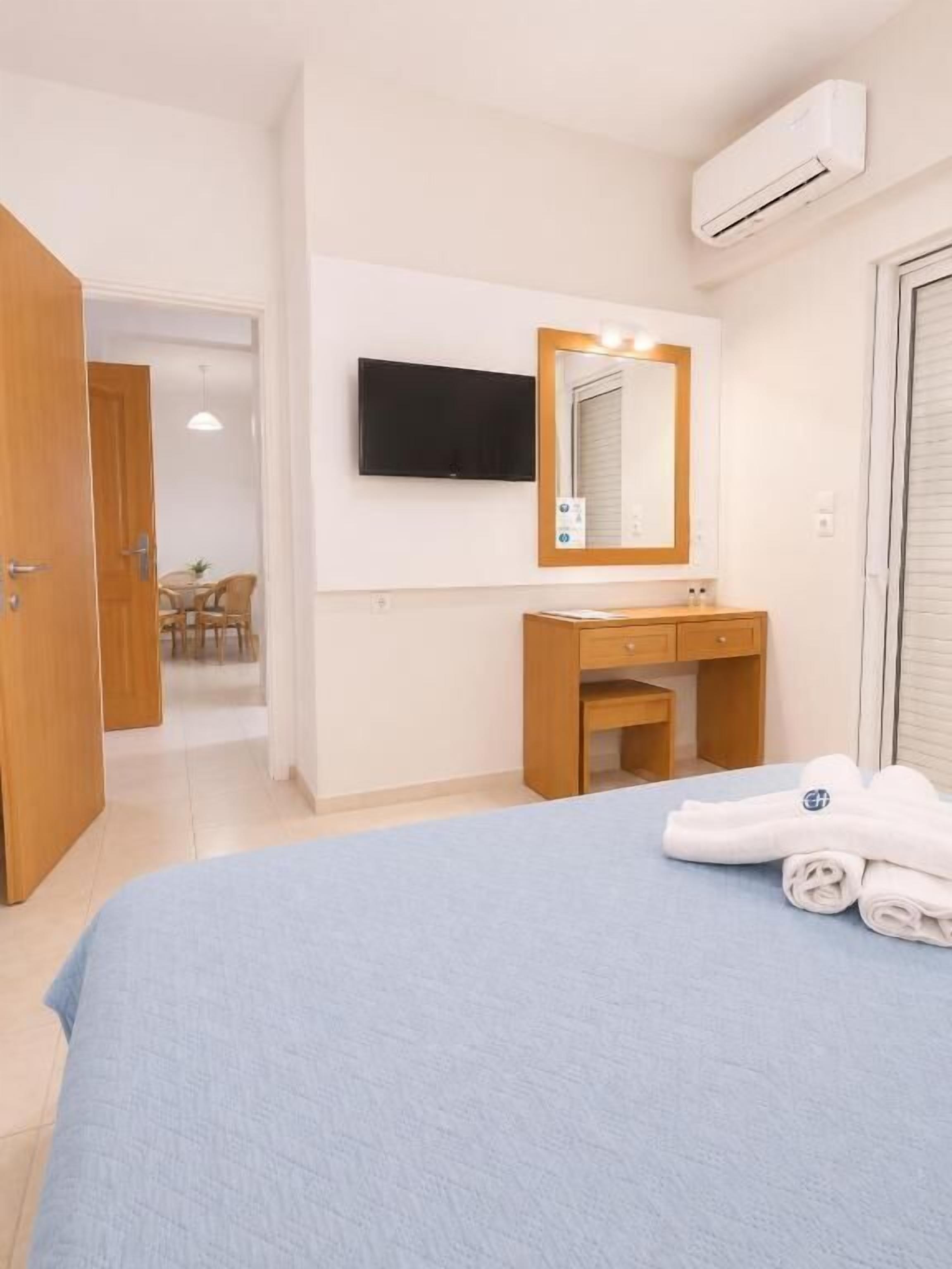 A hotel room with a bed, a bathroom with a mirror, a TV, and an air conditioning unit.
