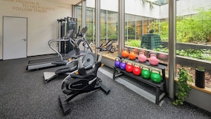 Un gimnasio moderno con equipo de ejercicio, una pared con mensajes motivacionales y vistas a zonas verdes a través de grandes ventanales.