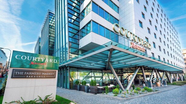 Un hotel Courtyard Marriott con entrada de vidrio, un letrero del Mercado de Agricultores y un camino pavimentado.