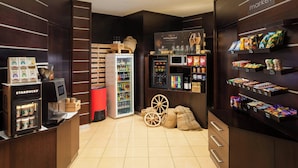 Un vestíbulo de hotel con una máquina de café Starbucks, un minibar, un refrigerador y una zona de mercado con snacks y bebidas.