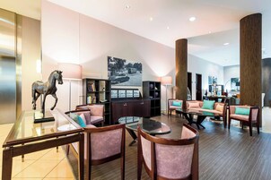 Una hall d'albergo moderna con un tavolino da caffè in vetro, sedute imbottite, una statua di cavallo e un'ampia immagine appesa al muro.