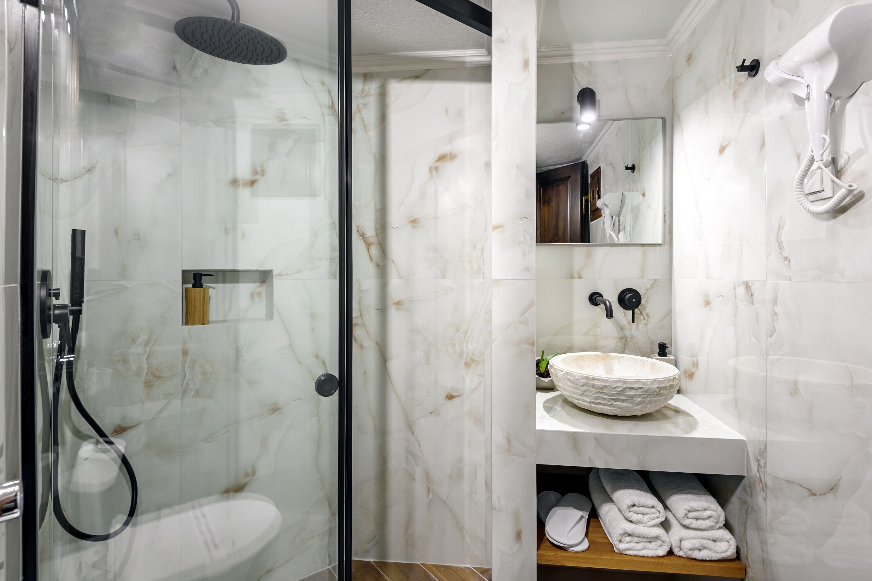 Un baño moderno con ducha de vidrio, lavamanos de mármol y espejo sobre el lavamanos.