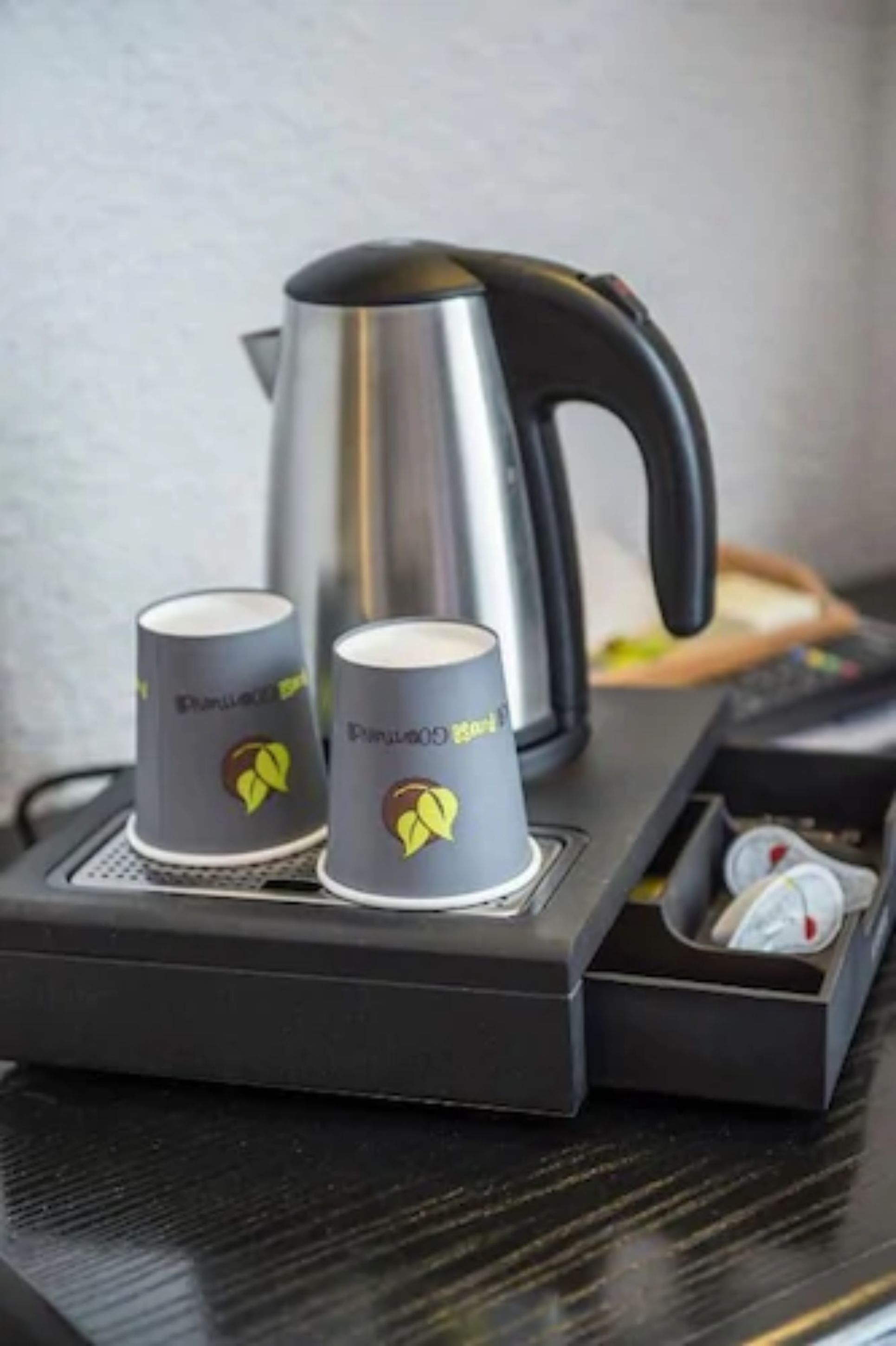 A coffee machine with two disposable cups on a tray, a kettle, and a control panel with knobs.