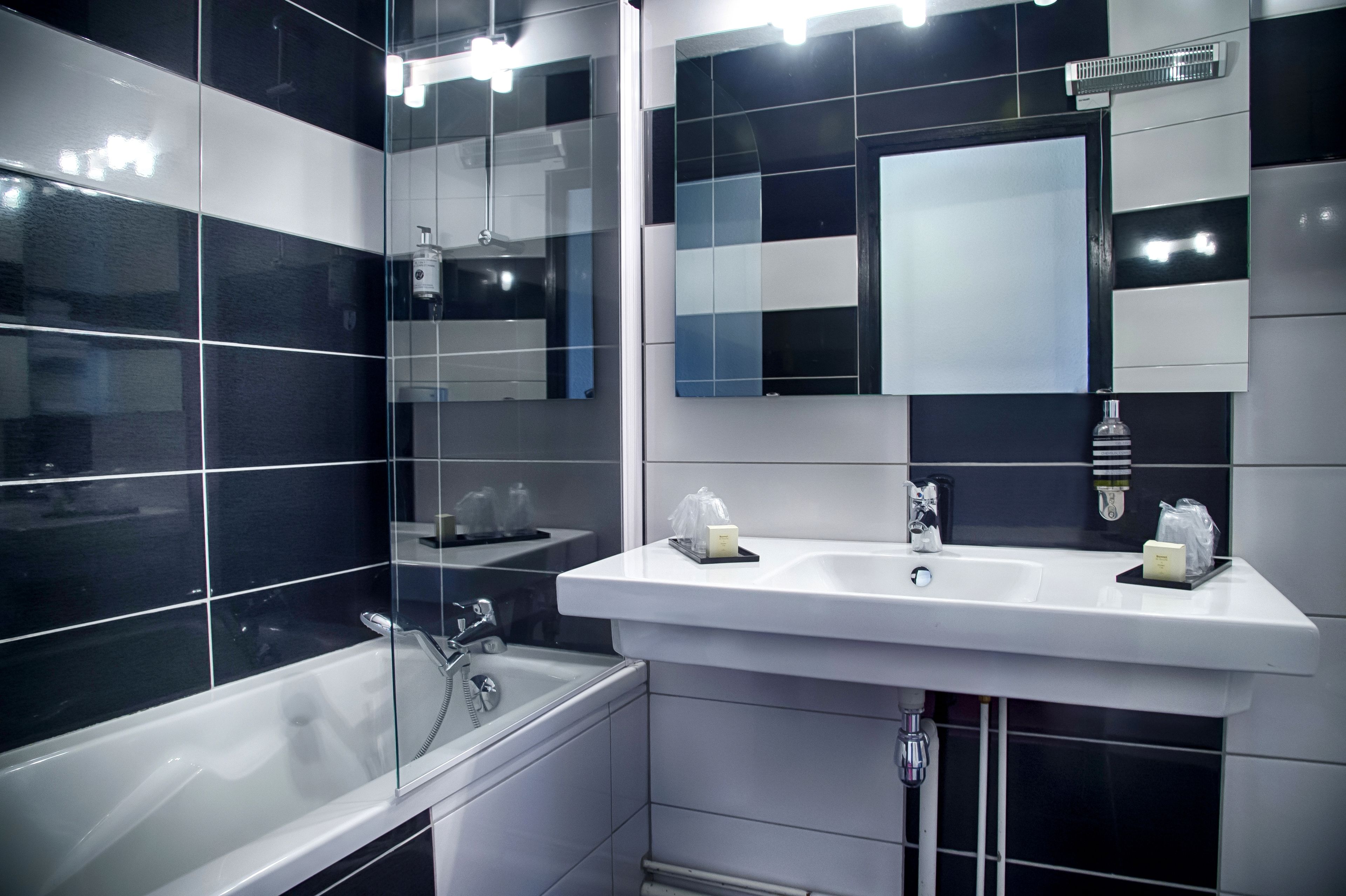 Une salle de bain moderne avec une douche à l’italienne en verre, un lavabo blanc doté de deux robinets et un grand miroir au-dessus du lavabo.