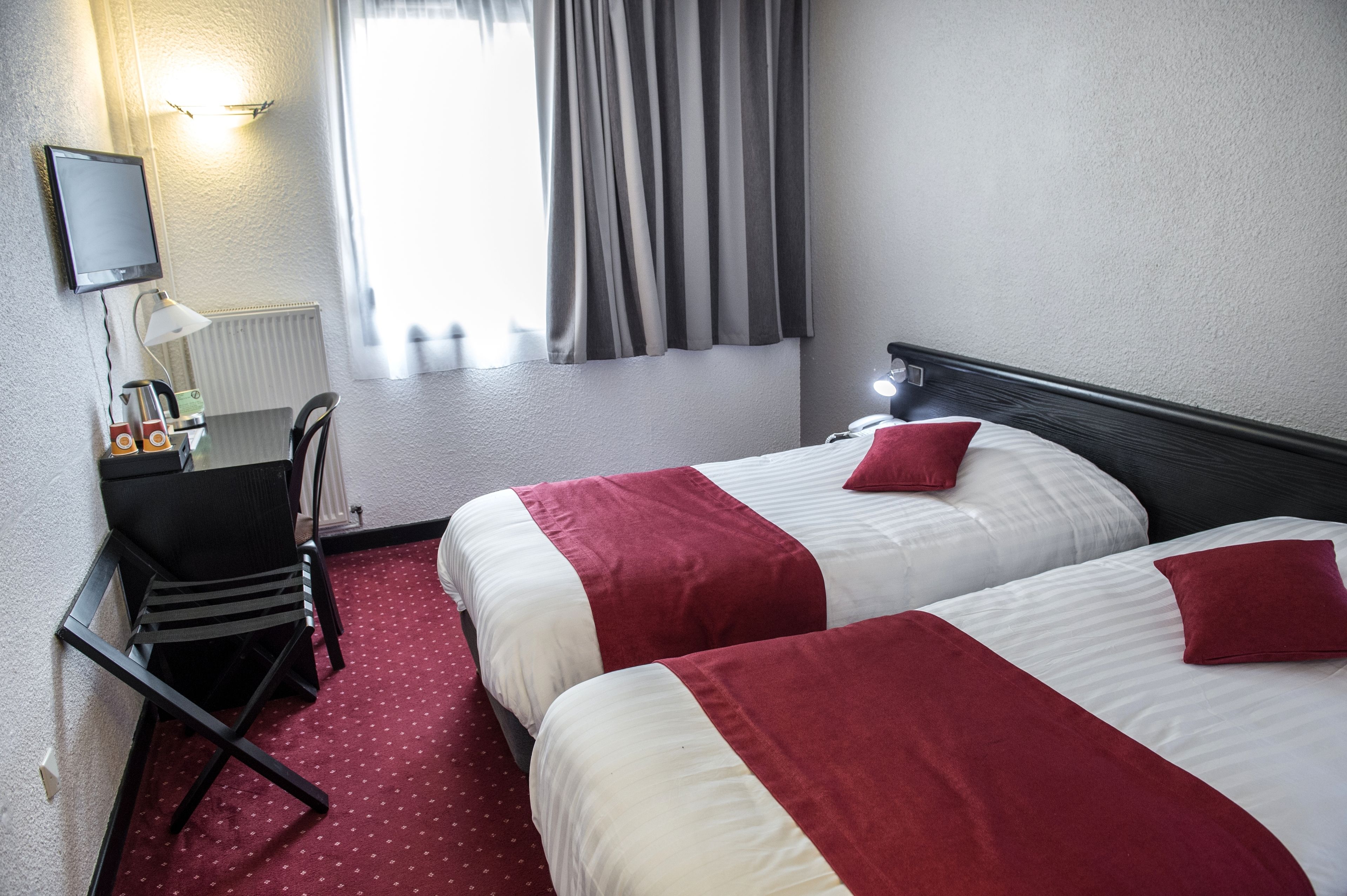 Een hotelkamer met twee bedden, een bureau, een stoel, een televisie en een raam met gordijnen.