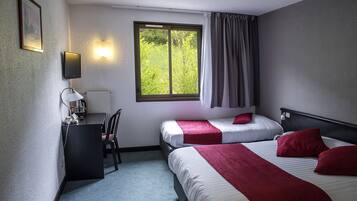 A hotel room with two beds, a desk, a chair, a window with curtains, and a wall-mounted lamp.