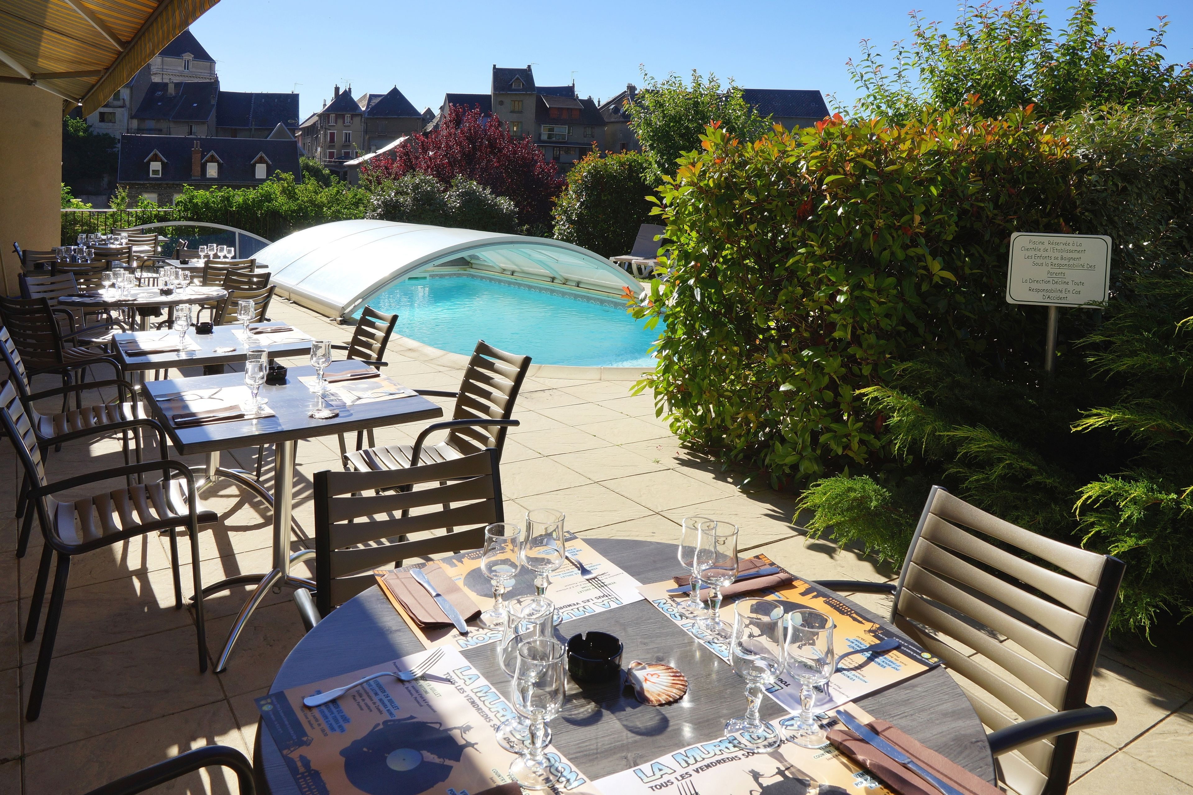 An outdoor dining area with tables set for a meal, a pool, and a view of the surrounding buildings.